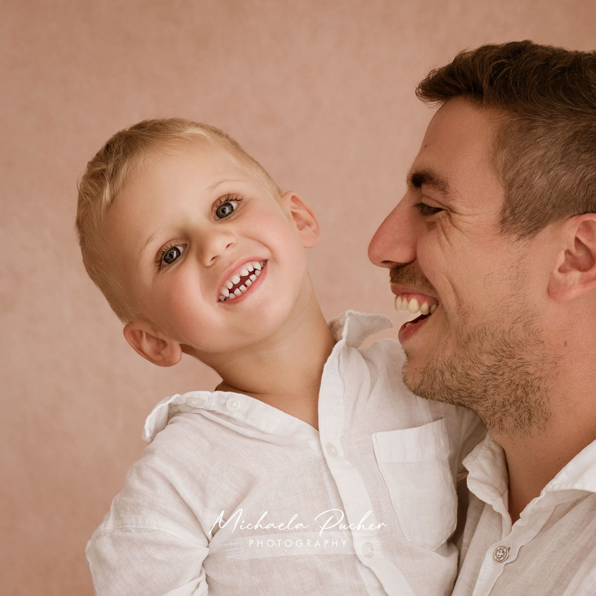 Vater hält seinen lachenden kleinen Sohn im Arm, beide schauen sich voller Freude an.